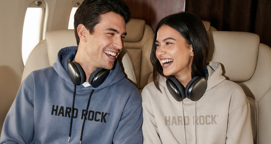 Smiling couple wearing Hard Rock hoodies with headphones, sitting together and laughing.