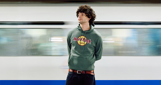 New Classic Logo Hoodies; A person wearing a Olive Green Hard Rock Classic Logo Hoodie looking left with a train moving behind him.