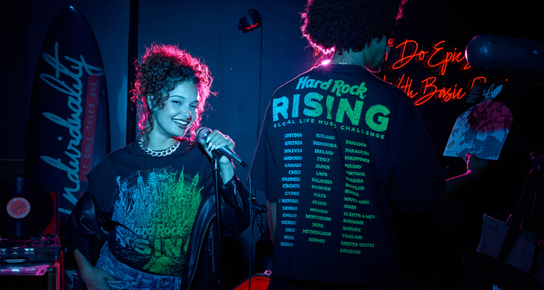 Two models wearing black Hard Rock Rising T-shirts, shown from the back and front, featuring colorful Hard Rock graphics.