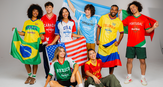 Group of six models in USA, Spain, Mexico, Colombia, and Argentina jerseys posed on a soccer field with a ball at center, showcasing the 2026 World Cup collection.